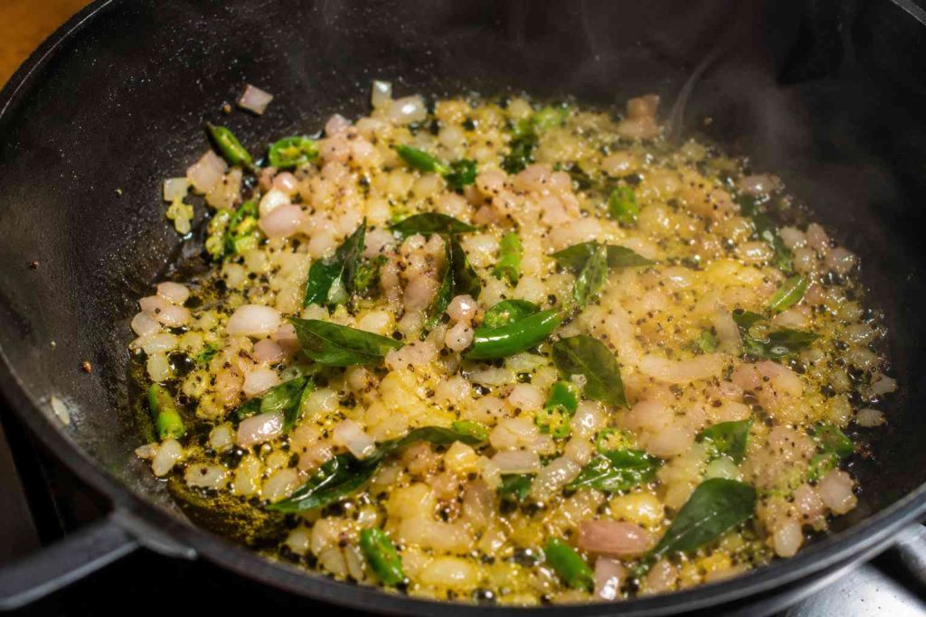 Preparing poha tadka with onions, curry leaves, and green chilies.