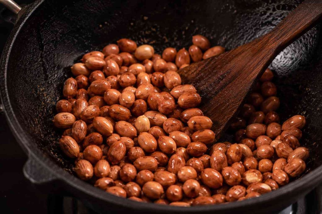 Close-up of roasted peanuts being stirred in a cast iron pan with a wooden spatula during cooking.